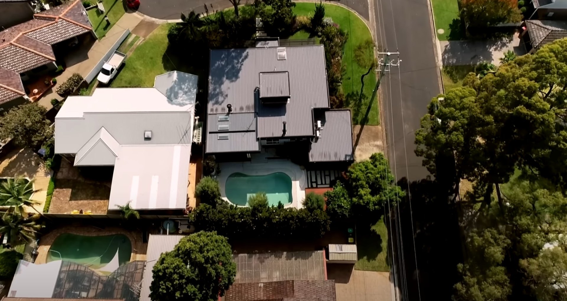 Aerial view of residential property with swimming pool, well-maintained lawn, and mature landscape design in suburban setting