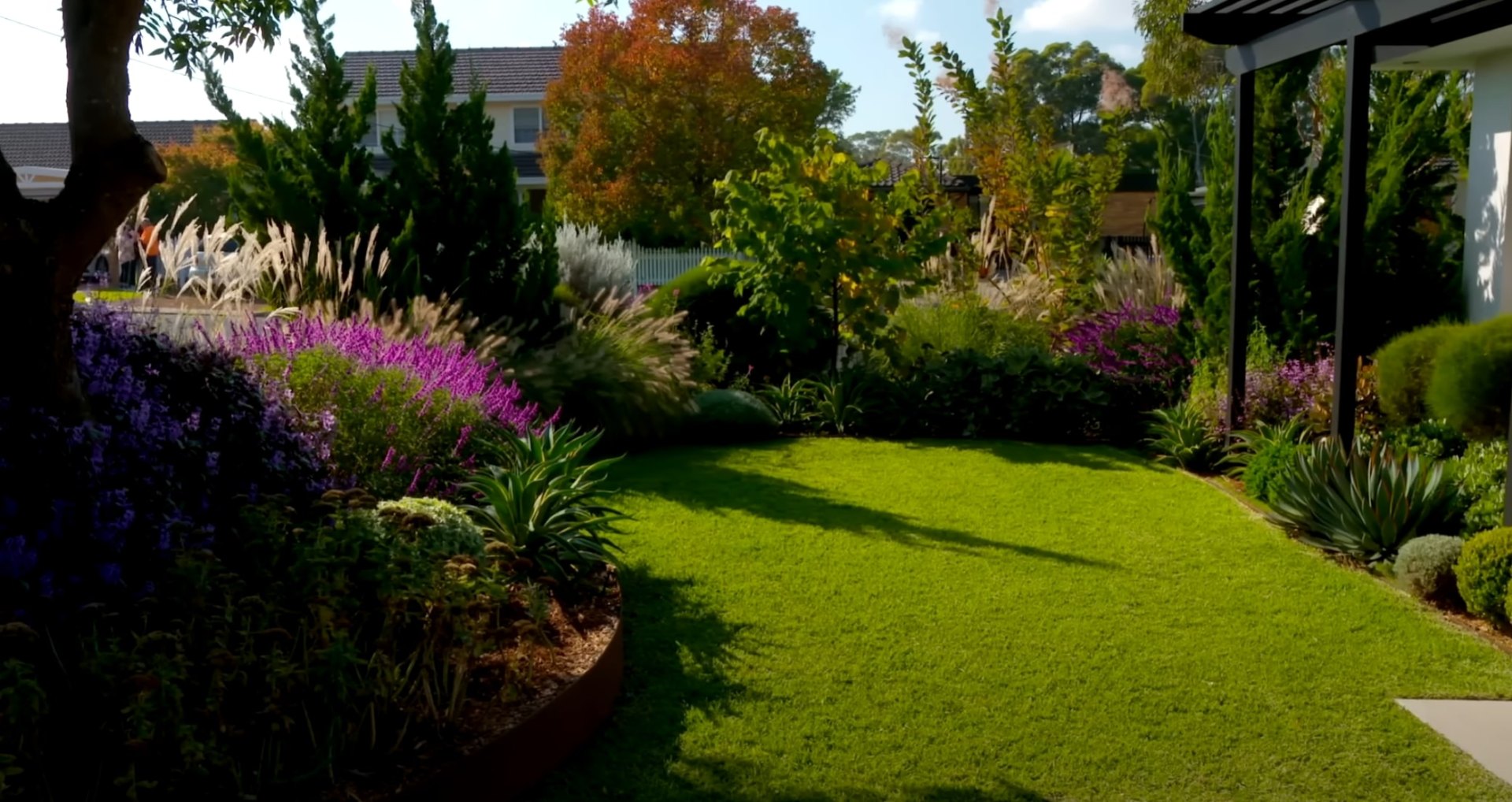 Beautiful garden landscape with vibrant purple and green plantings, ornamental grasses, and well-maintained lawn areas