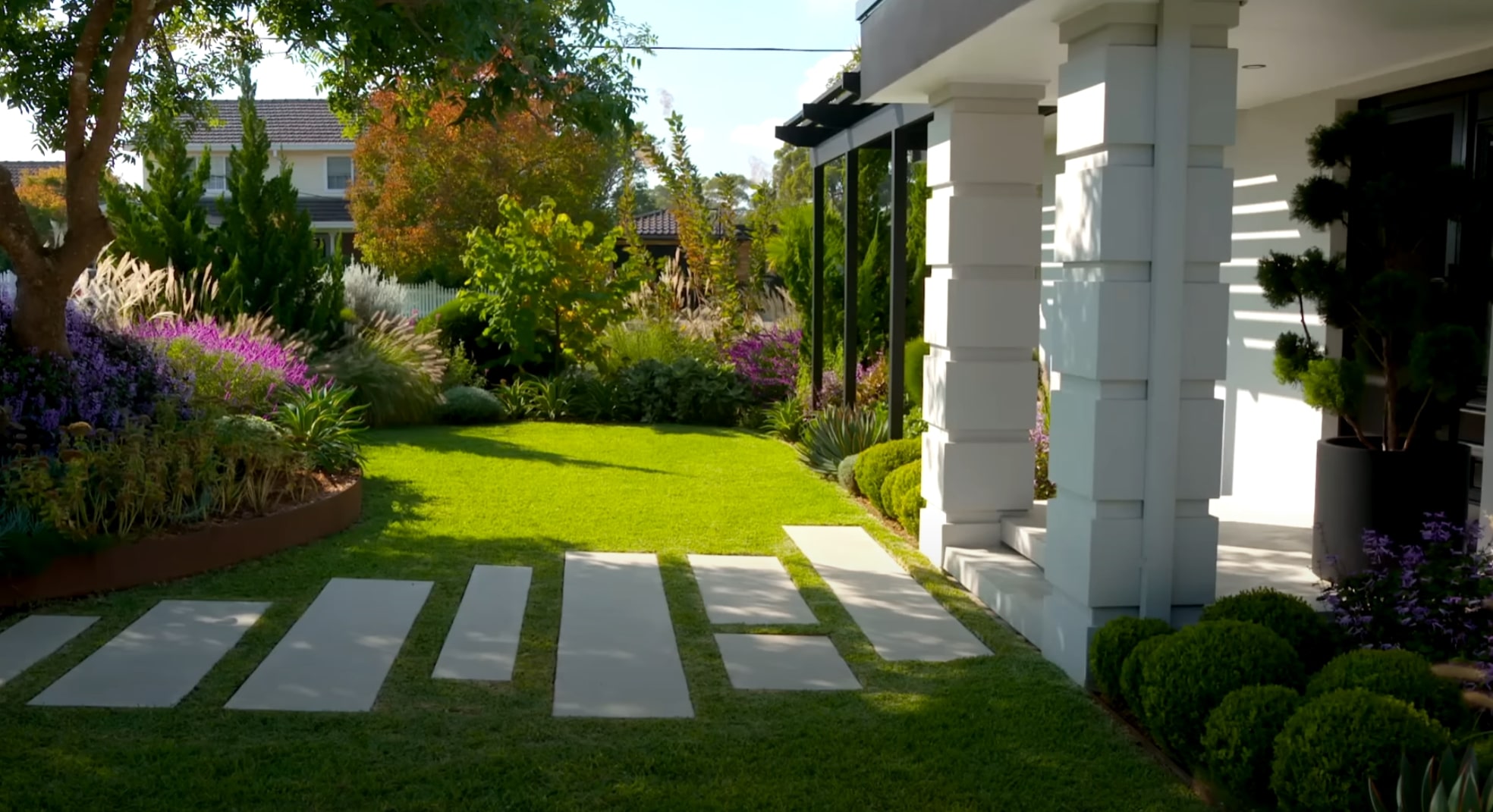 Elegant front yard landscape with concrete stepping stones, lush lawn, colorful perennial borders, and modern architectural elements