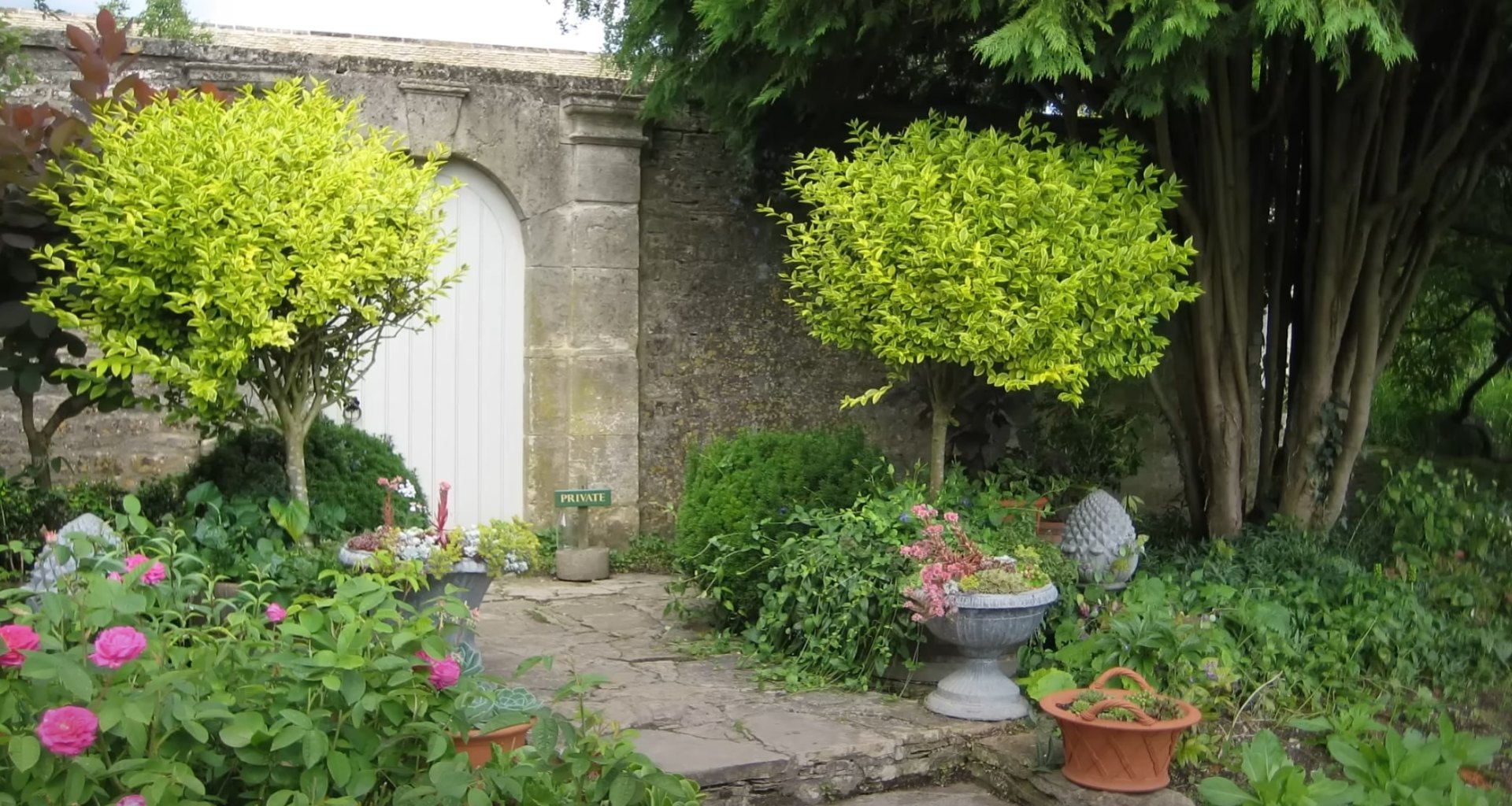 Elegant garden entrance with stone gate posts, ornate metal gate, and lush landscaping in established outdoor living area